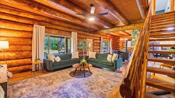 A log cabin interior with a green sofa set, a coffee table, and a stone wall.
