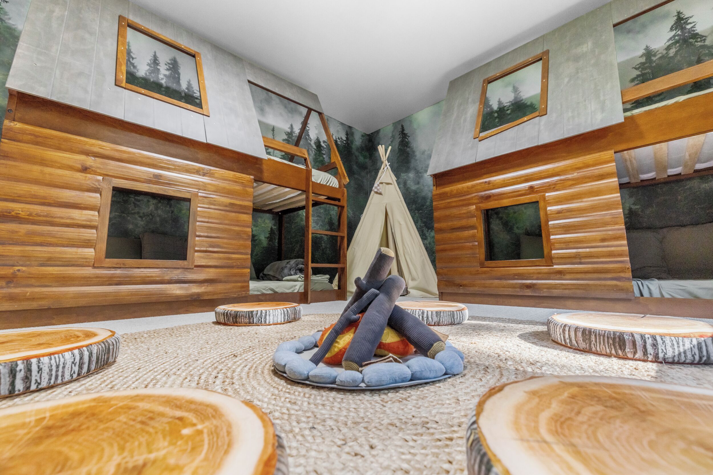 Une pièce comprenant un lit superposé, une tente tipi et un espace de détente circulaire avec des tables rondes en bois.