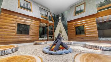 Une pièce comprenant un lit superposé, une tente tipi et un espace de détente circulaire avec des tables rondes en bois.