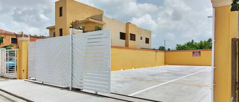 Un área de estacionamiento con acceso restringido y un edificio amarillo al fondo.