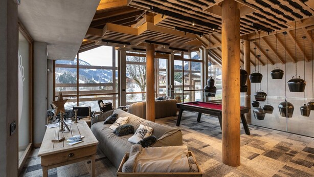 Una habitación acogedora con una mesa de billar, asientos cómodos y amplios ventanales con vistas a las montañas.