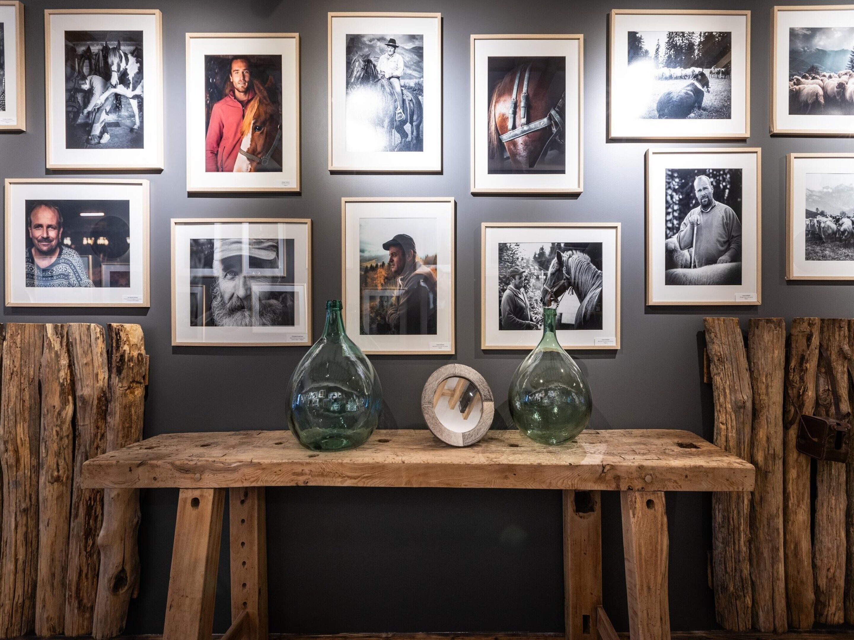 A wall with framed photographs and two green glass bottles on a wooden table.