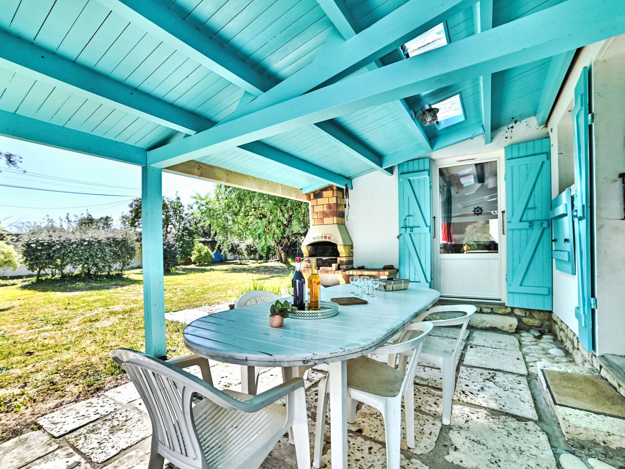 Um pátio externo com mesa e cadeiras redondas, um forno de tijolos e uma porta azul.