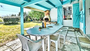 An outdoor patio with a round table and chairs, a brick oven, and a blue door. - La Sablière by Interhome (Ile d'Oléron)
