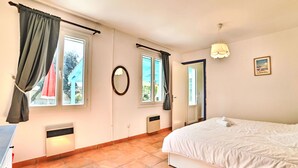 A bedroom with a bed, two windows with curtains, a mirror, a radiator, and a picture on the wall. - La Sablière by Interhome (Ile d'Oléron)