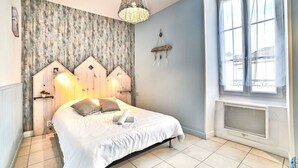 A bedroom with a bed, a wooden headboard, a hanging light fixture, a window with curtains, and a radiator. - Cheray 1 by Interhome (Ile d'Oléron)