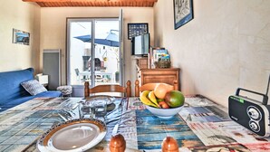 Una habitación acogedora con techo de madera, una mesa de comedor dispuesta con platos, vasos y un cuenco de fruta. Hay un sofá azul, un televisor y un radio en la mesa.