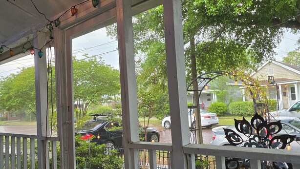 A covered porch with string lights, a white railing, and a view of parked cars and houses. - Charming, 1-bedroom in downtown Wilmington! (Wilmington)
