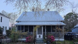 A two-story house with a porch, surrounded by a black metal fence and flowering plants. - Charming, 1-bedroom in downtown Wilmington! (Wilmington)