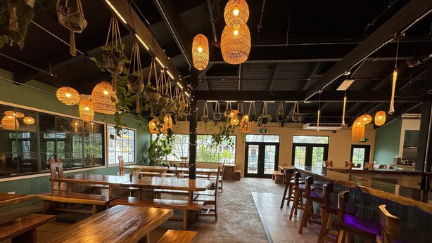 A restaurant with wooden tables and benches, hanging wicker lamps, and large windows.