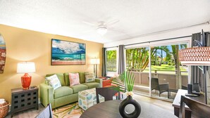 A living room with a green sofa, a coffee table, and a painting of a beach scene. - Plantation Hale D2 "The Palm Shade Stay" – Newly Renovated with AC (Kapaa)