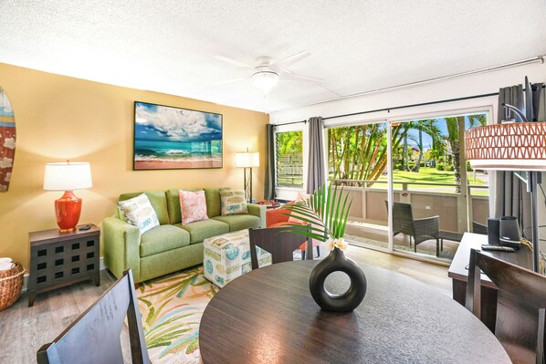 A living room with a green sofa, a coffee table, and a painting of a beach scene.