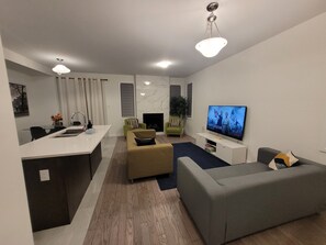 A modern living room with a grey sofa, a beige sofa, a TV, and a fireplace. - Venetian Retreat: Golf, Concerts, Hockey or Work Offsite (Ottawa)