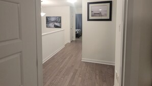 A hallway with wooden flooring, white walls, and two framed pictures.