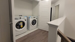 A laundry room with two front-loading washing machines, a white door, and a wooden floor.