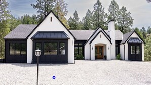 A modern house with a symmetrical design, featuring a central entrance, large windows, and a gravel driveway.
