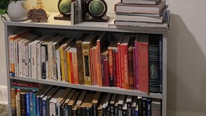 Ein Bücherregal mit verschiedenen Büchern, einer Lampe, einem Globus und einem gerahmten Bild an der Wand.