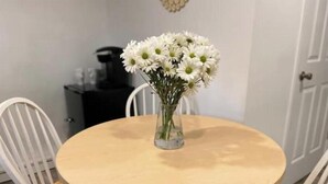 Ein runder Holztisch mit einer Vase weißer Blumen in der Mitte, umgeben von weißen Stühlen.