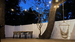 Une terrasse extérieure avec une plateforme en bois, un fauteuil suspendu et une table entourée de chaises.