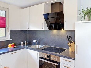 A modern kitchen with white cabinets, a black countertop, a built-in stove, and a sink.