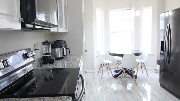 Una cocina moderna con armarios blancos, encimera de granito, refrigerador de acero inoxidable y una zona de comedor con una mesa redonda y sillas.