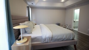 Una habitación de hotel moderna con una cama grande, mesitas de noche, una lámpara y vistas al baño.