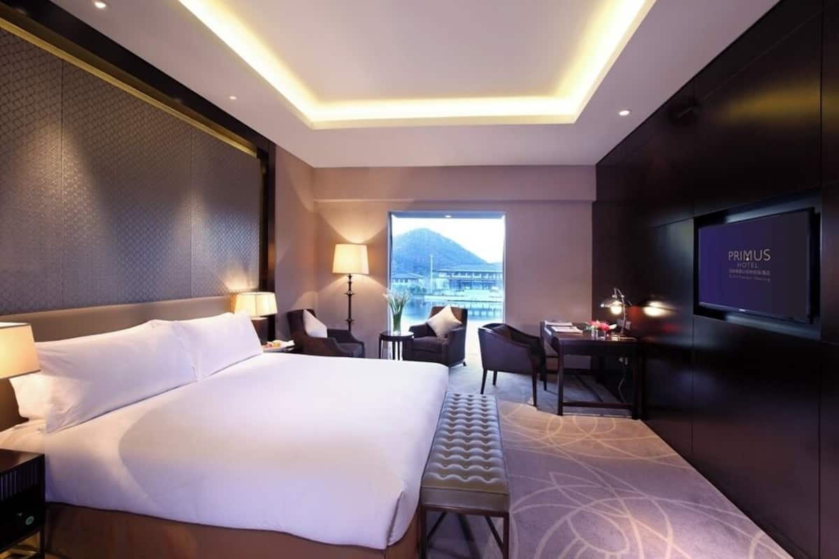 Una habitación de hotel moderna con una cama grande, un escritorio con silla, un televisor y vistas a la montaña.