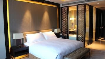 Una habitación de hotel moderna con una cama grande, mesitas de noche, un banco y un separador decorativo.