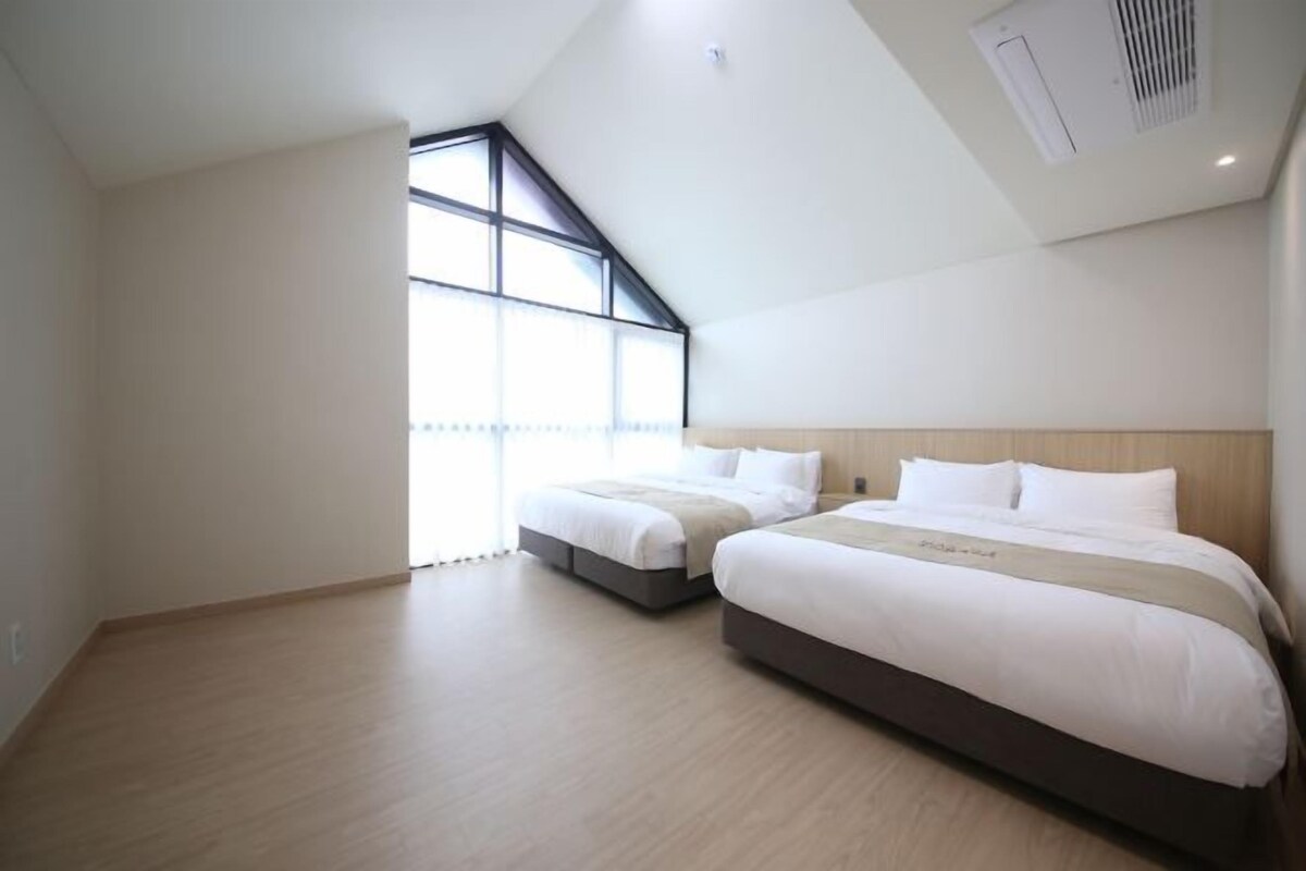 Ein Hotelzimmer mit zwei Betten, einer schrägen Decke und großen Fenstern.