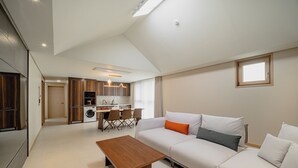 Een ruime woonkamer met een bank, een houten salontafel en een keuken op de achtergrond.