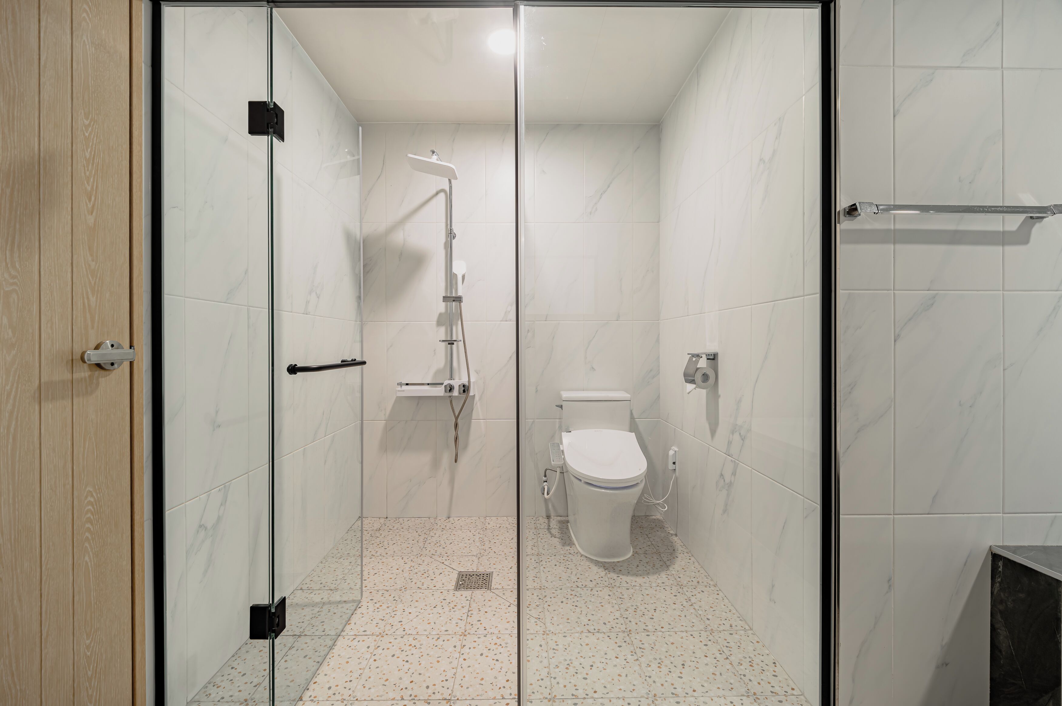 Een moderne badkamer met een glazen douchecabine, een toilet en een vloer betegeld met marmer.
