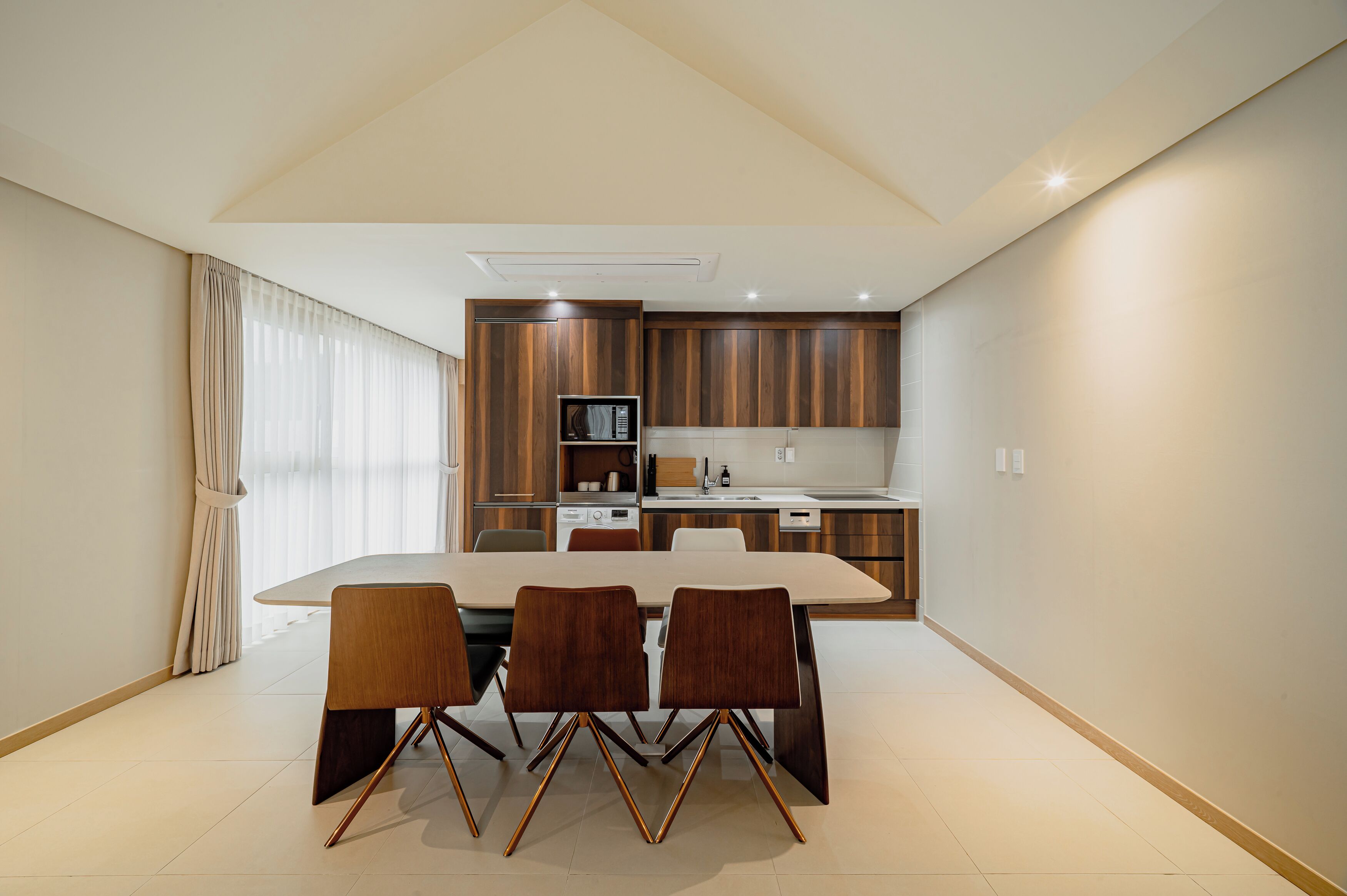 Una cocina moderna con armarios de madera, una mesa de comedor con sillas y un amplio ventanal con cortinas.