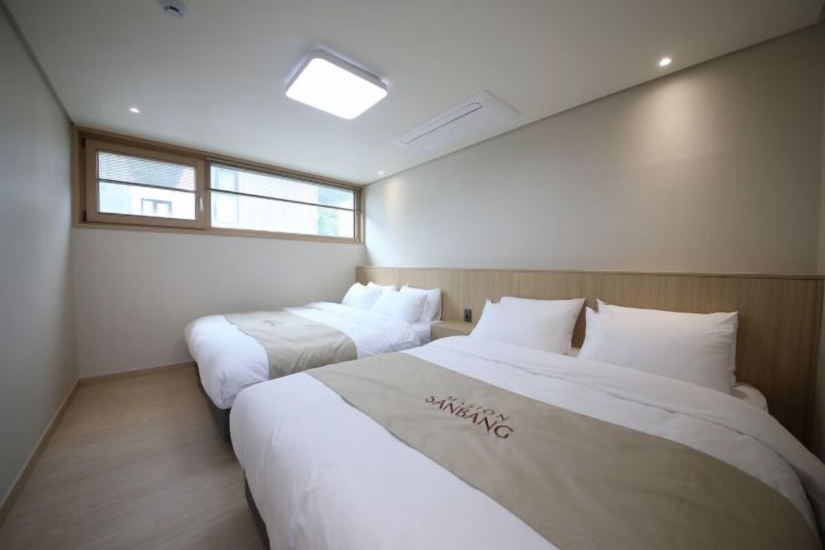 A hotel room with two beds, a large window, and a ceiling light.