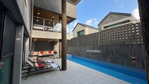 Een modern zwembadterras met ligbedden en een houten omheining.