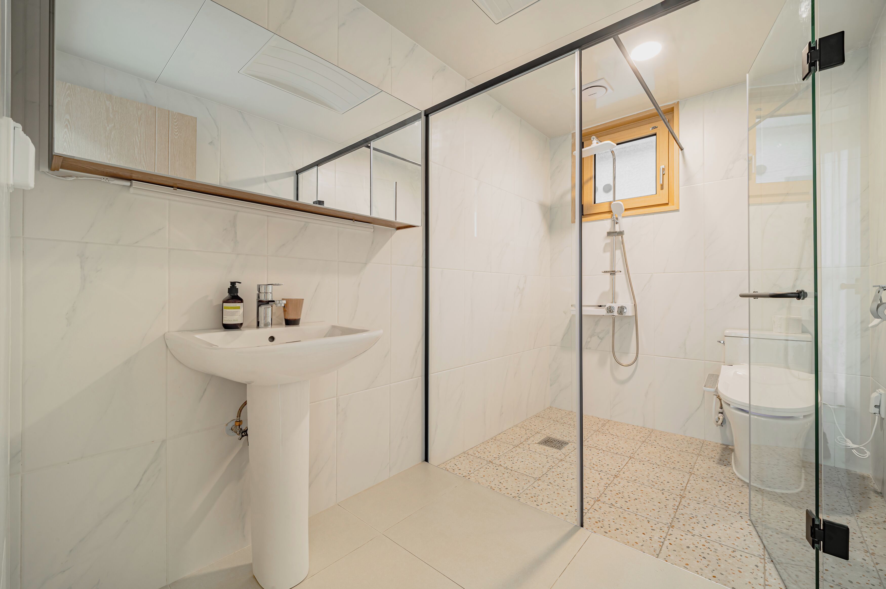 A modern bathroom with a glass-enclosed shower, a white sink, and a wooden shelf above the mirror.