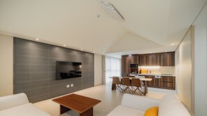 Een moderne woonkamer met een flatscreen televisie, een houten salontafel en een bank met een geel kussen.