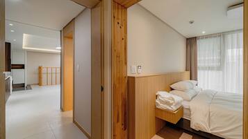 A modern hotel room with a wooden headboard, a neatly made bed, and a view of the city through large windows.