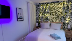 Een slaapkamer met een bed, een nachtkastje, een lamp, een foto aan de muur en een muur met klimop en verlichting.