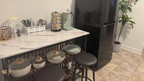 Een keuken met een zwarte koelkast, een koffiezetapparaat, een plant en barstoelen.