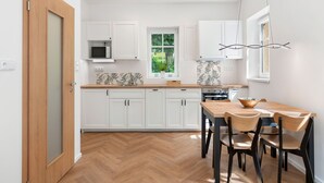 Une cuisine moderne avec des meubles blancs, un parquet en bois disposé en motif chevron et un coin repas comprenant une table et des chaises en bois.