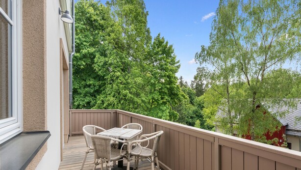 Une terrasse en bois, agrémentée d’une table et de chaises, entourée d’une balustrade en bois, et offrant une vue sur un paysage verdoyant et luxuriant.
