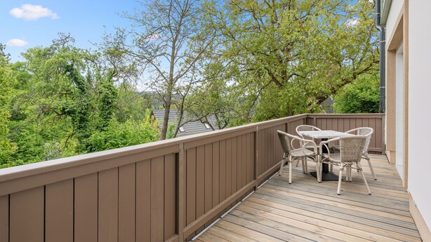 A wooden deck with a table and chairs, surrounded by a brown fence, overlooking a lush green landscape. - V kapradí by Interhome (Hřensko)