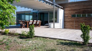 Et moderne hus med en overdækket terrasse, spiseplads og en facade af træ.