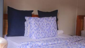 A bed with a patterned blue and white blanket, a dark blue pillow, and a plain white pillow.