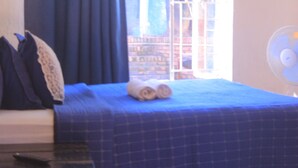 Habitación de hotel con una cama, un ventilador y vistas a un edificio de ladrillo.