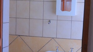Un baño con lavamanos pedestal blanco, un mueble espejo y suelo de baldosas.