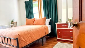 Un dormitorio con cama, cómoda, mesita de noche y ventana con cortinas.
