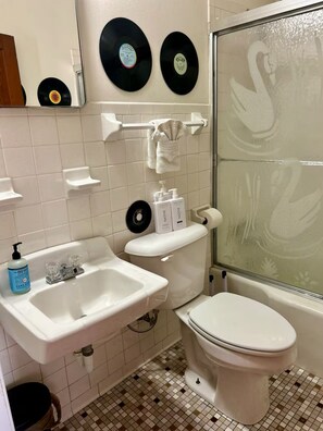 Ein Badezimmer mit Toilette, Waschbecken und Dusche. Über der Toilette befinden sich zwei Schallplatten an der Wand.