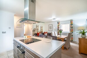 Eine moderne Küche mit Kochinsel, Edelstahlgeräten und einer Dunstabzugshaube mit Glasfront.