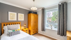A bedroom with a bed, a wardrobe, a nightstand, a window with curtains, and two framed artworks on the wall.